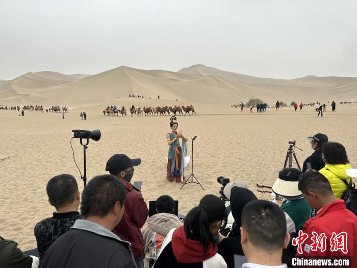圖為2023年4月底，敦煌大漠“逐舞者”奧楠在鳴沙山月牙泉景區(qū)視頻直播，吸引游人圍觀?！●T志軍 攝
